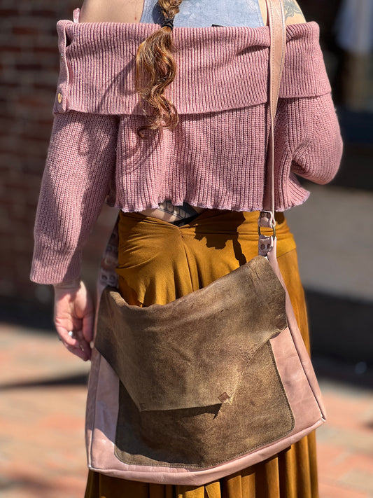 A person wearing a pink sweater and a brown messenger bag with gray accents.