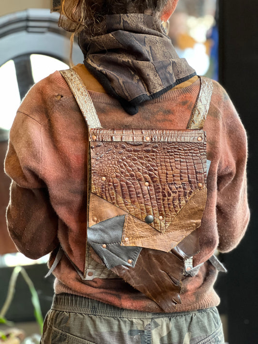 A person wearing a rustic gator embossed leather backpack with a patchwork design consisting of various leather styles.