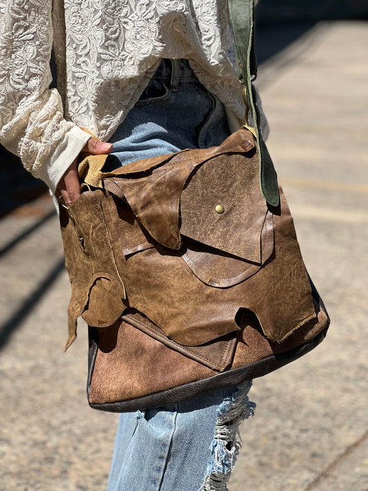 A person wearing a white shirt carrying a brown layered soft leather satchel bag over their shoulder.