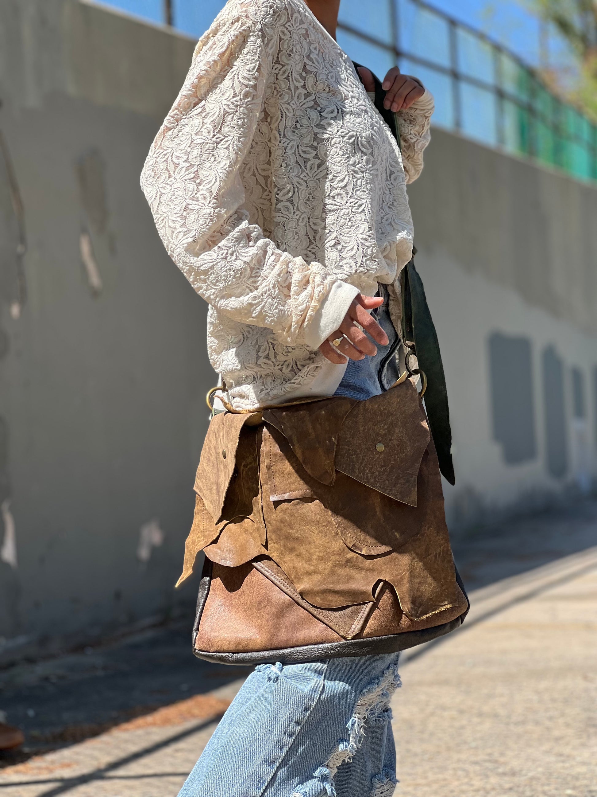 Person holding a brown leather bag outdoors.