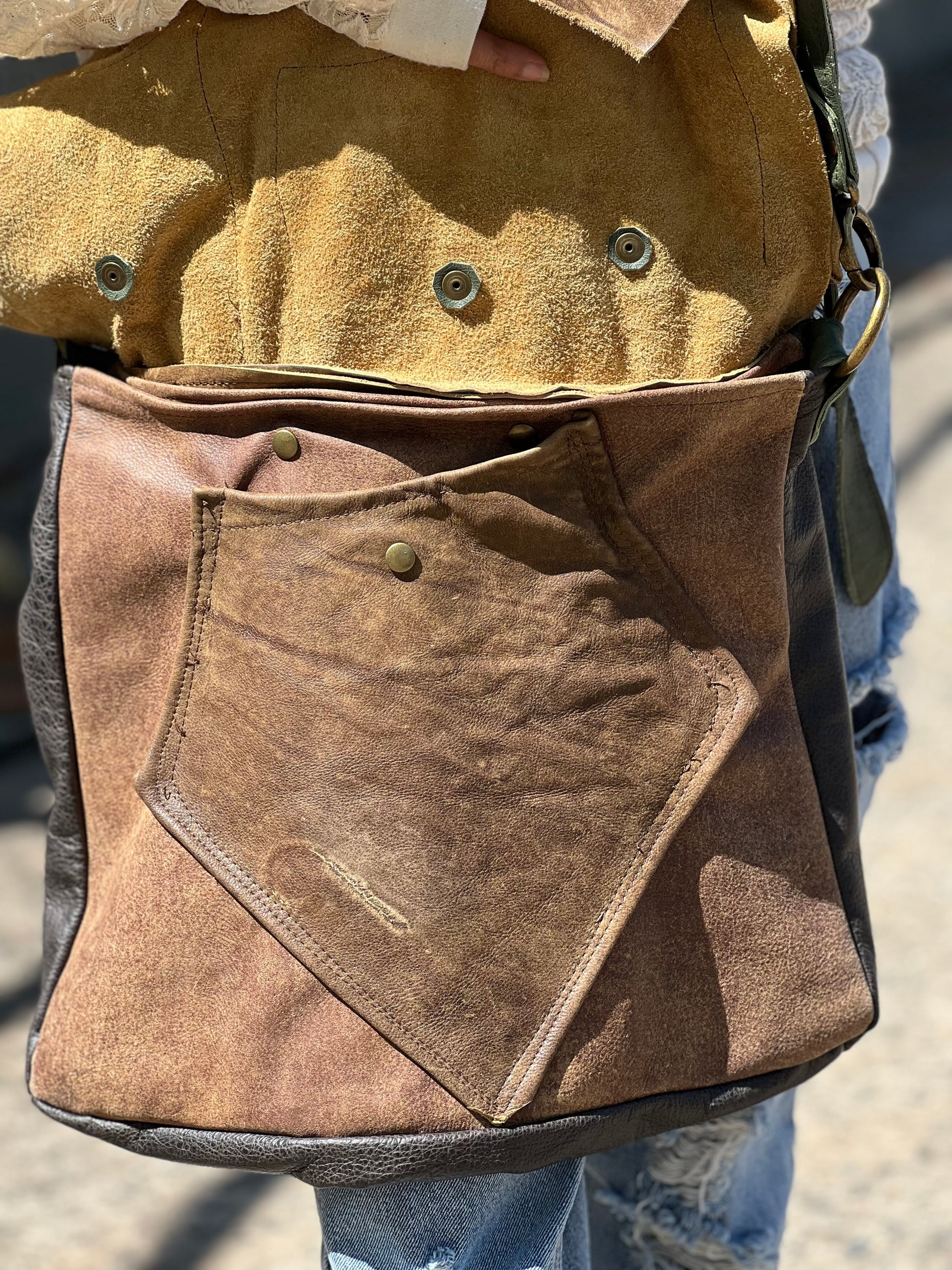 Close-up of a brown leather bag with buttons and a flap.