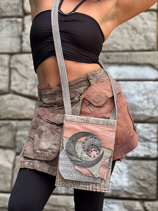 A person wearing a crossbody bag with a crescent moon design on a pink and brown leather strap.