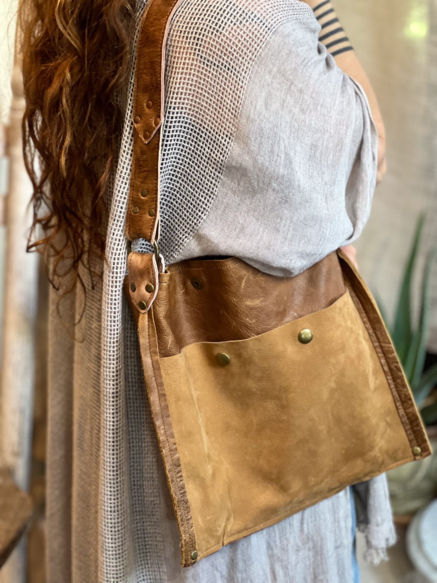 Person wearing a brown leather crossbody bag with a mesh side panel.