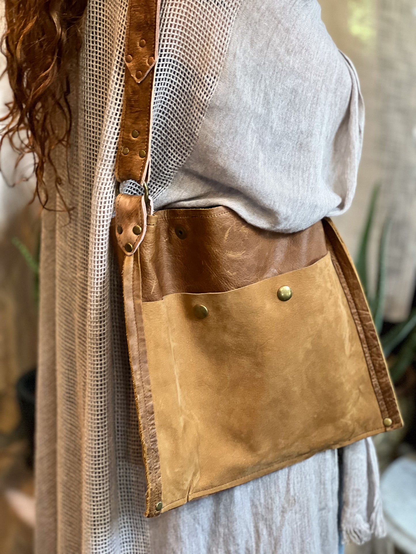 Brown leather bag with gold accents worn over a light-colored outfit.