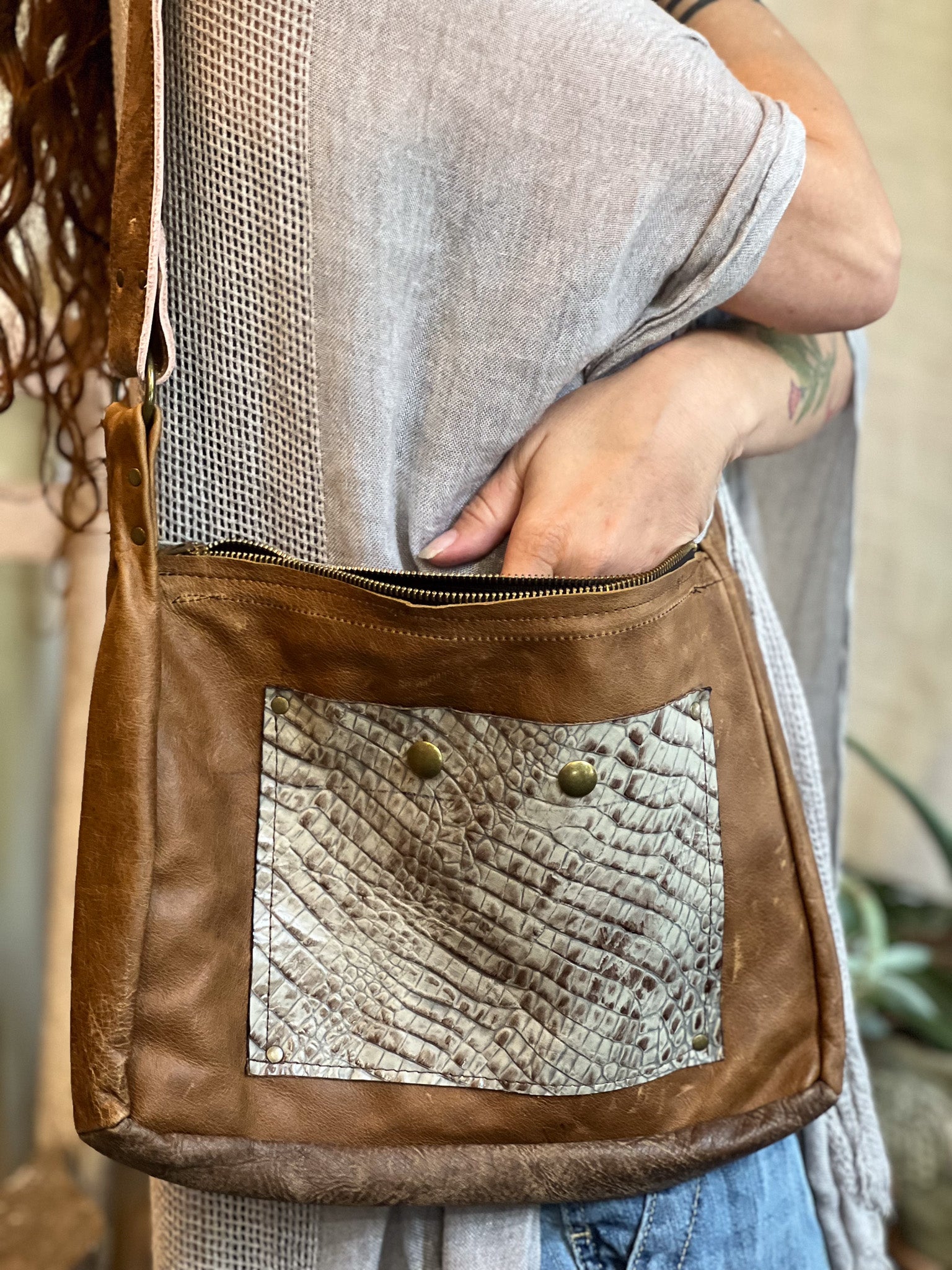 Brown leather crossbody bag with textured patch held by a person.