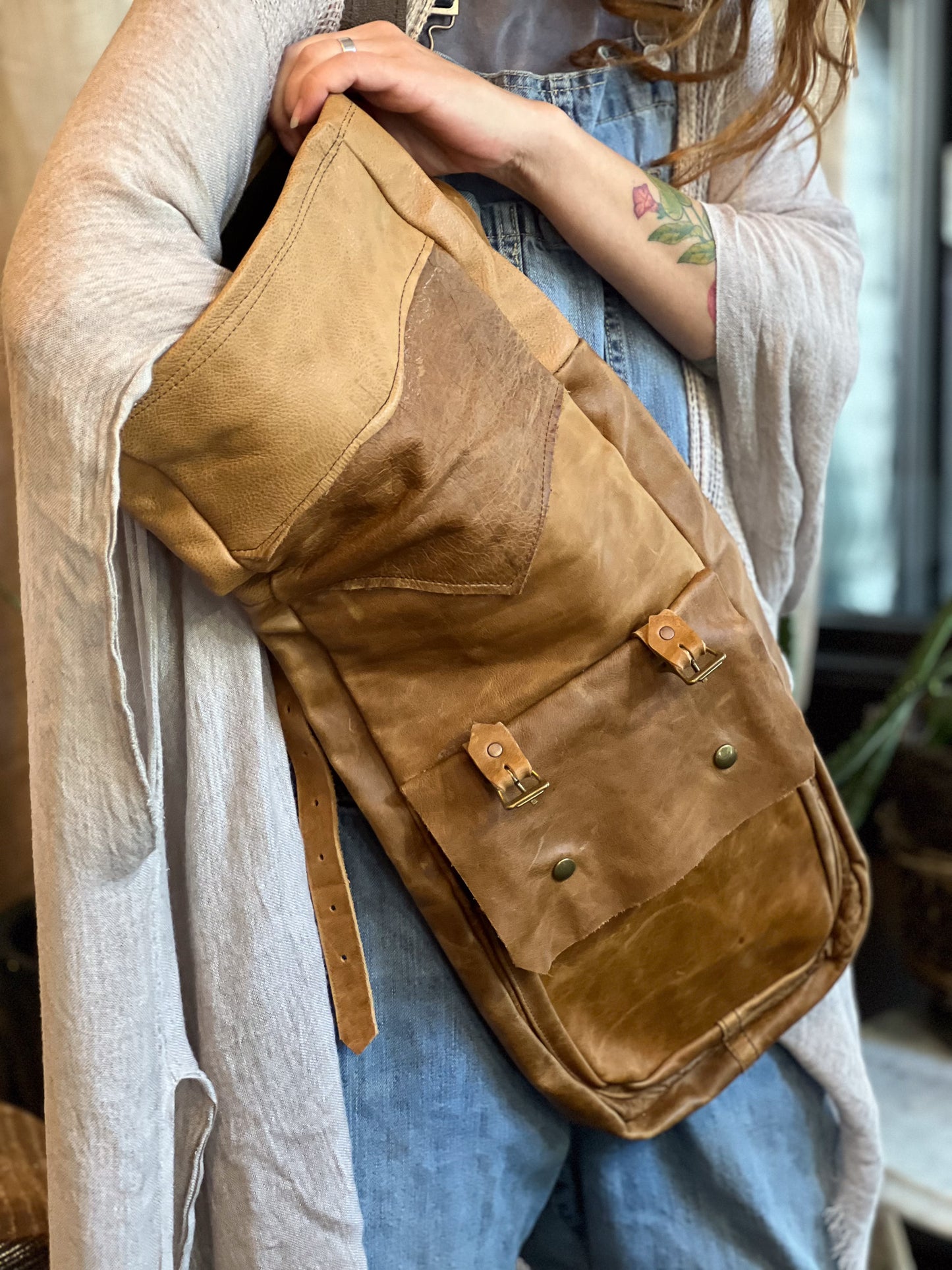 Brown leather bag held by a person wearing a light-colored shirt and blue jeans.