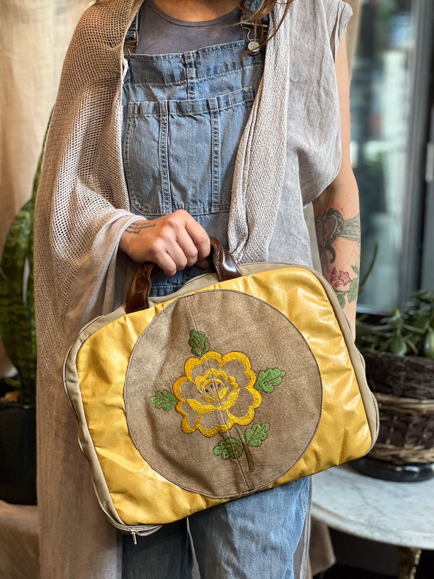 Person holding a yellow bag with floral embroidery in an indoor setting