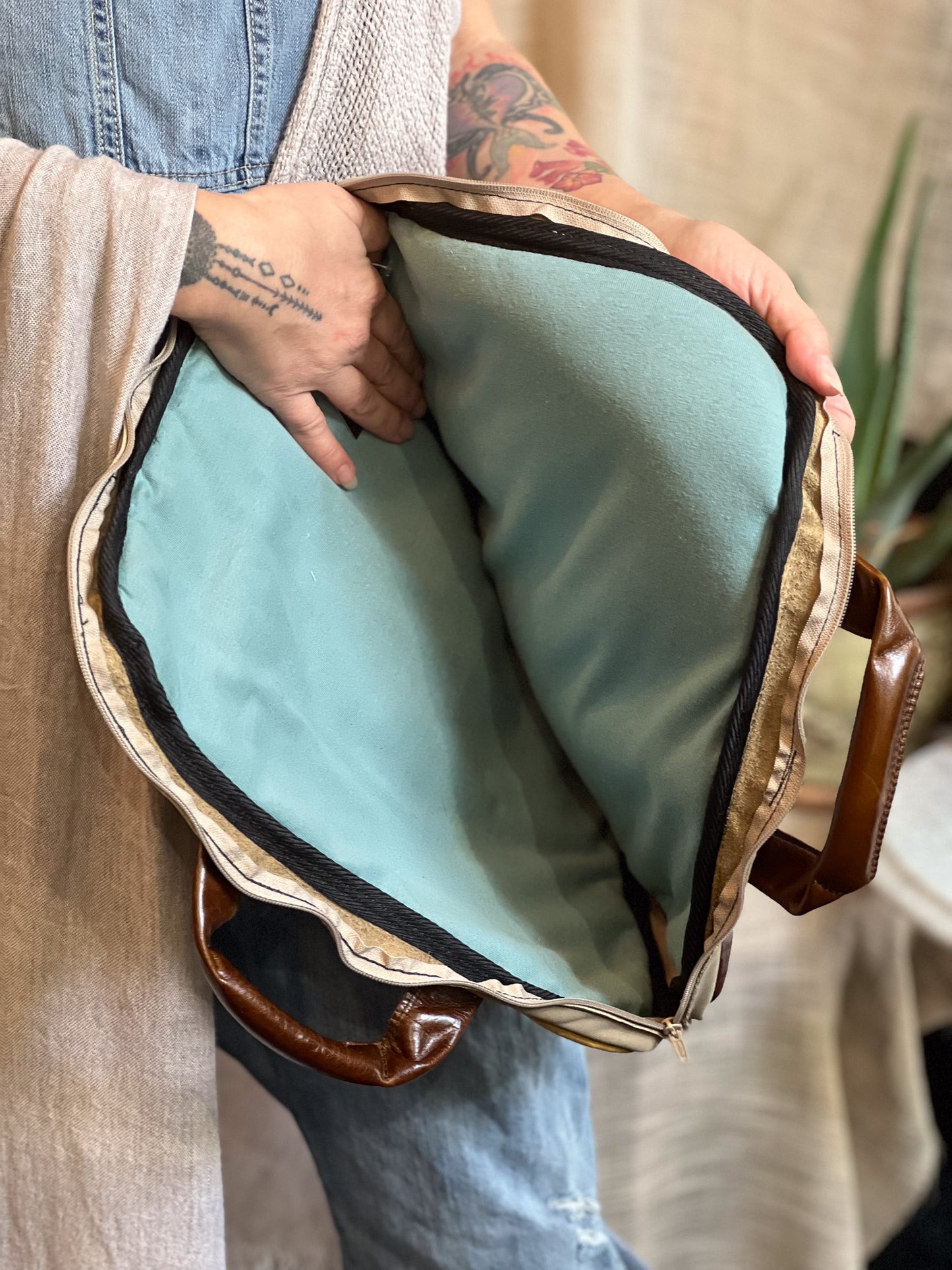 Person holding a brown leather bag with a light blue interior