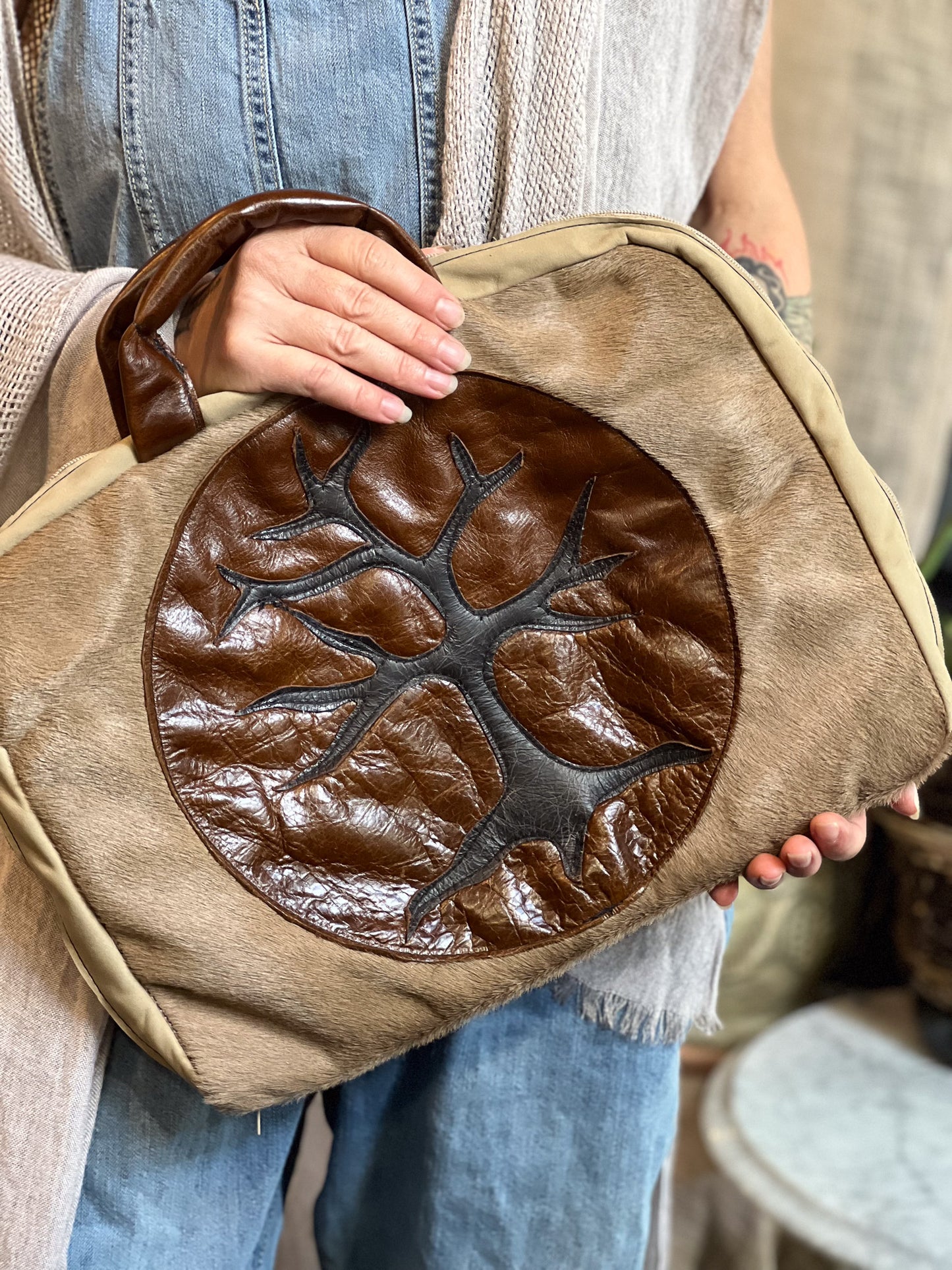 Person holding a brown leather bag with a tree design