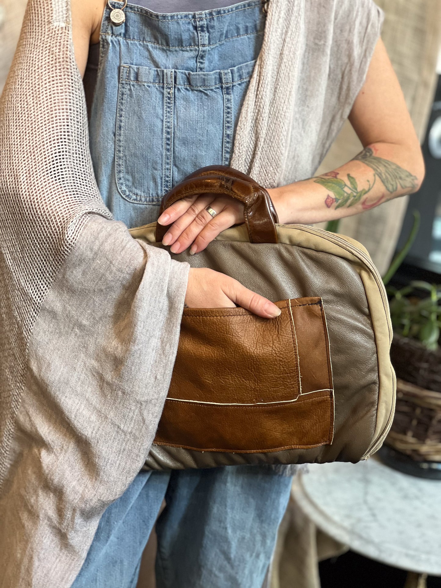 Person holding a brown and beige leather bag with denim overalls and a beige cardigan.