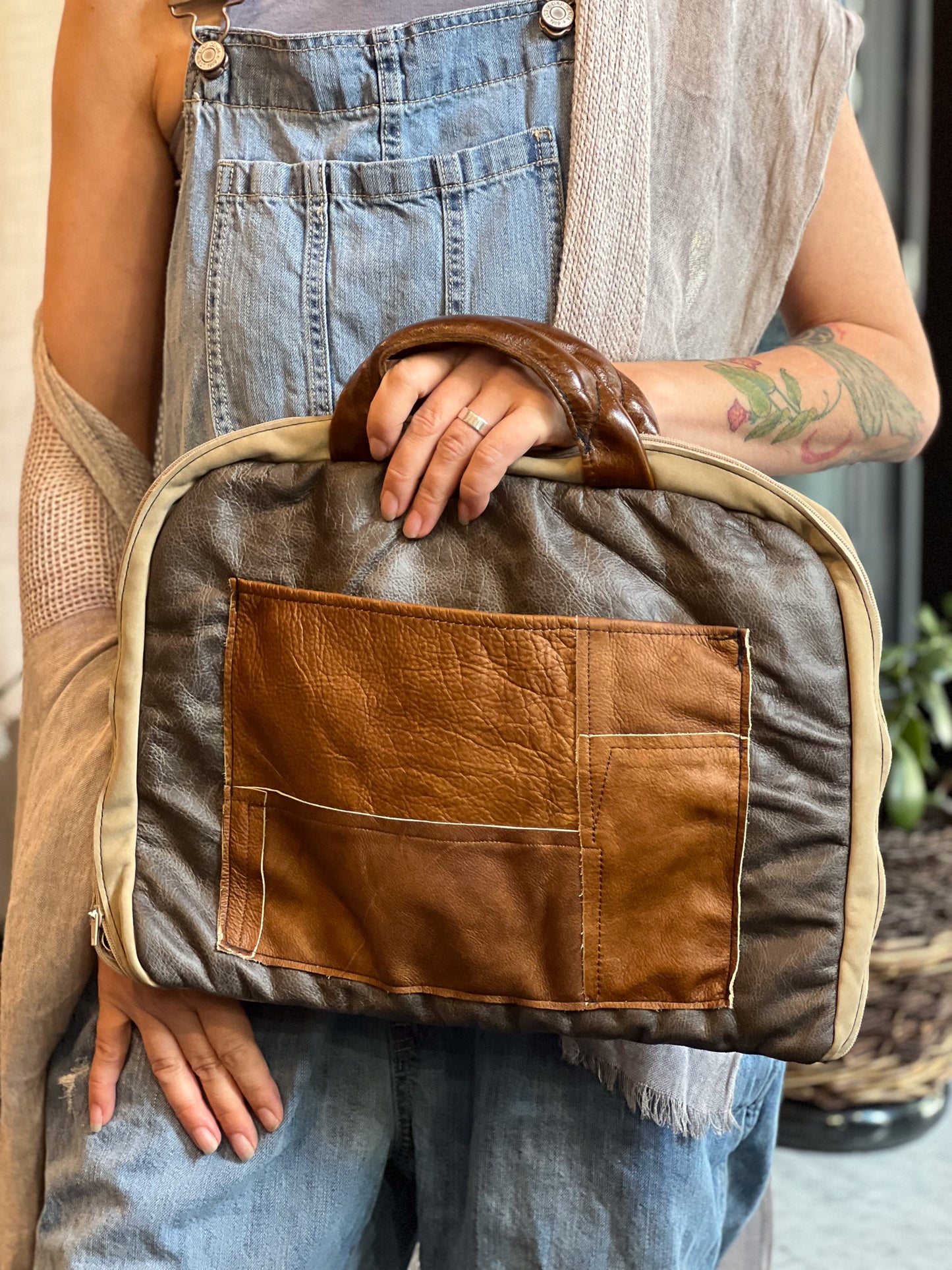 Person holding a brown and beige leather bag with denim overalls