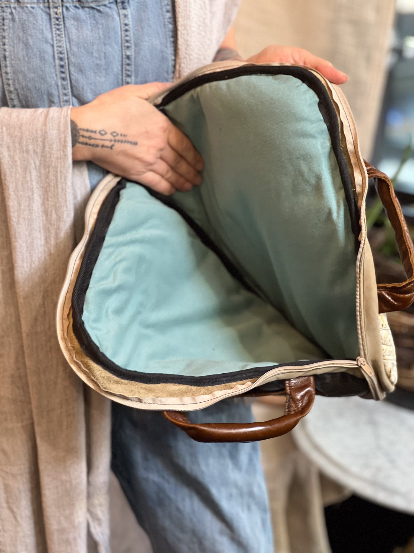 Person holding a light blue cushion inside a beige bag with brown handle.