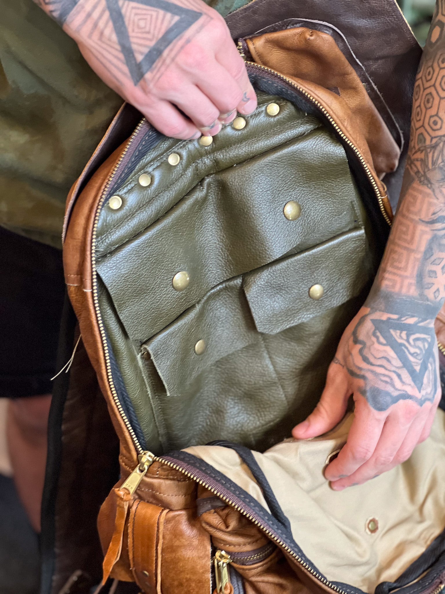 Close-up of a person opening a leather bag with visible tattoos on their arms.