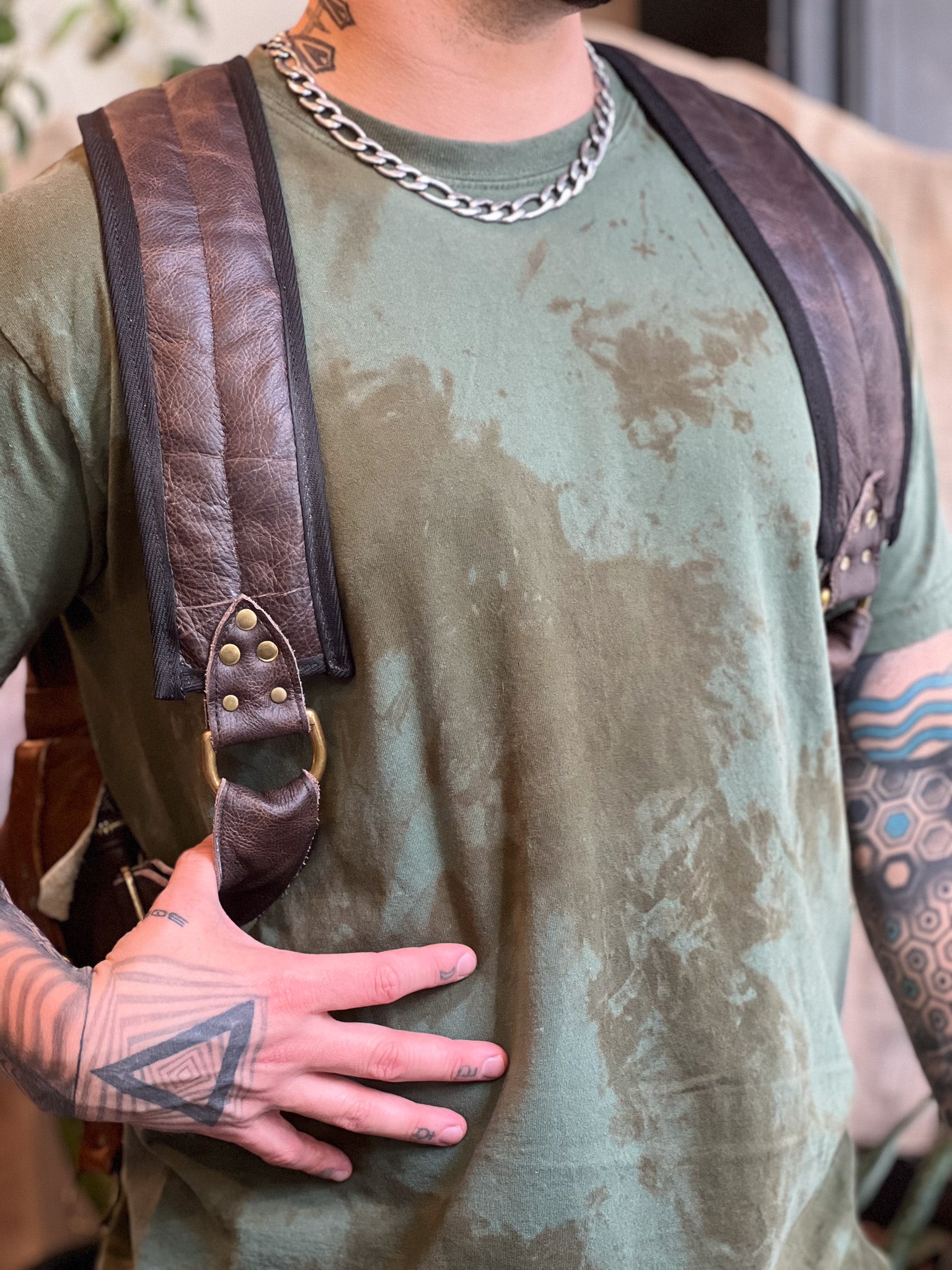 Person wearing a green distressed t-shirt with leather straps over shoulders