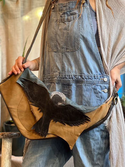 Person wearing a denim apron holding a brown leather bag with a bird design.