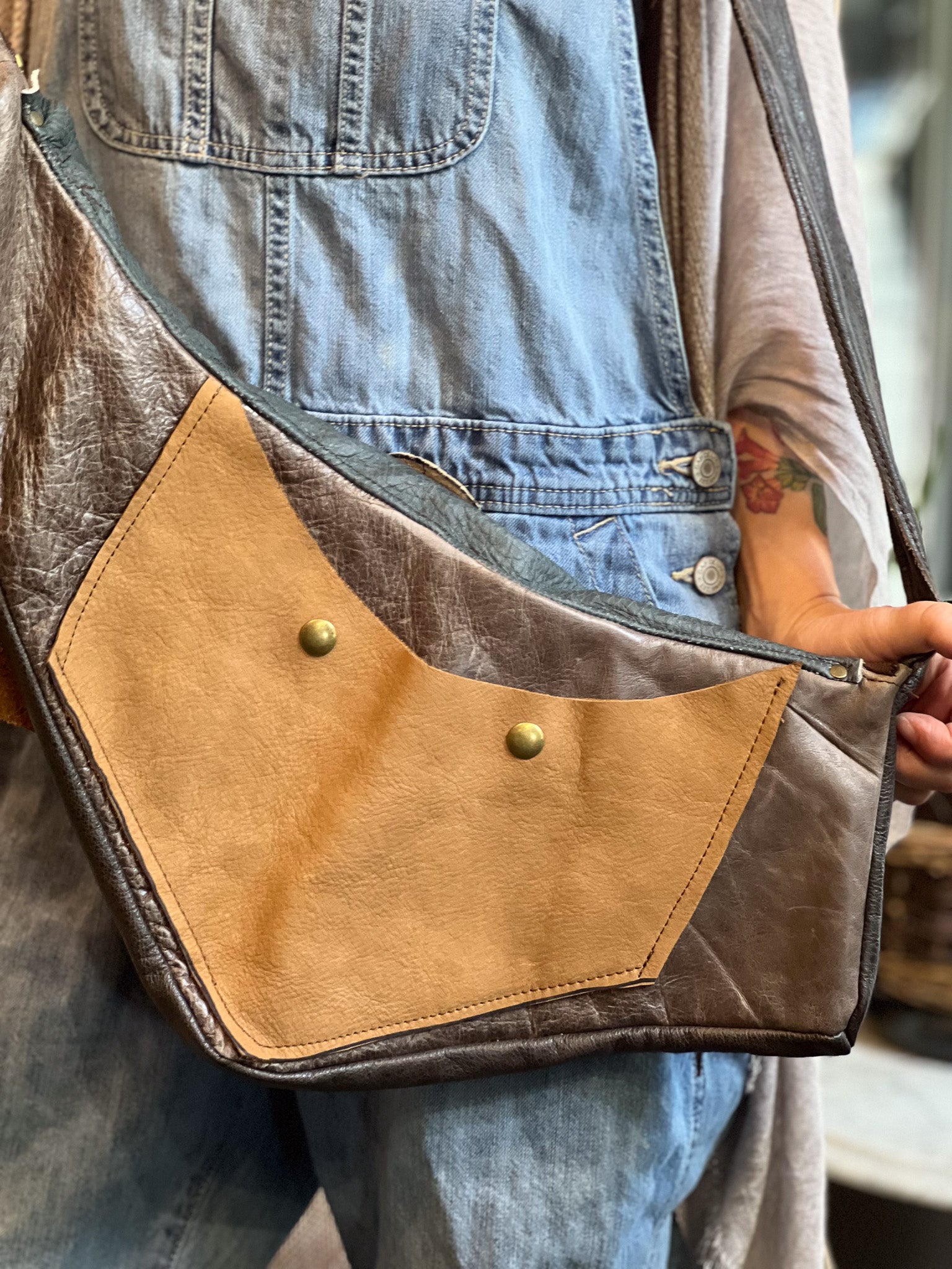 Person wearing a brown leather crossbody bag with denim overalls.