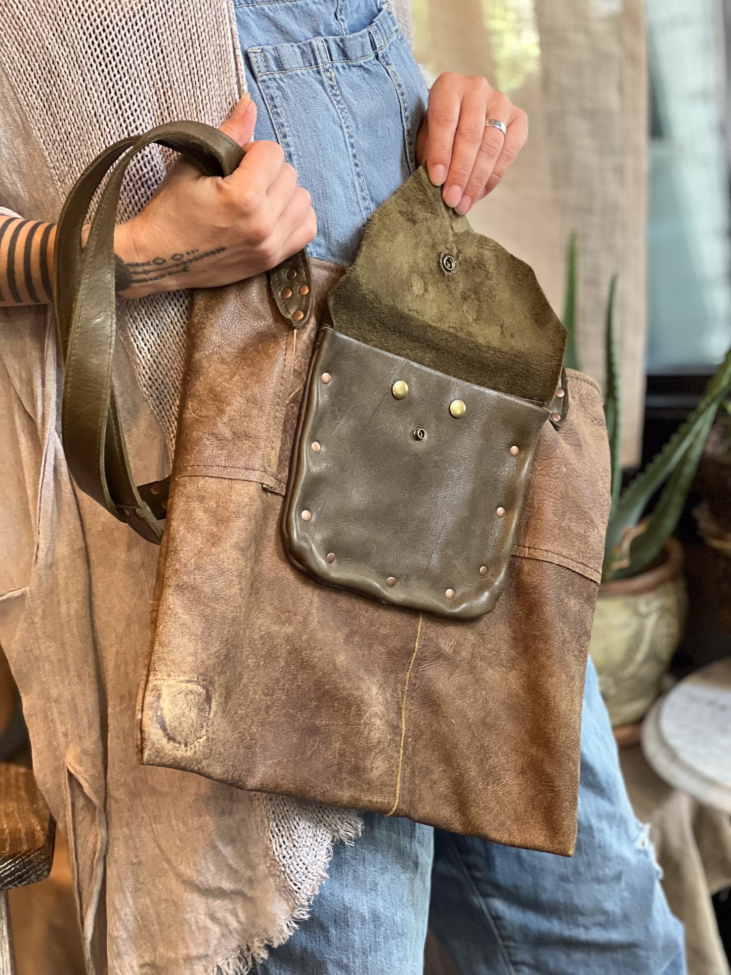 Person holding a brown leather bag with a pocket, wearing a beige jacket and blue jeans.