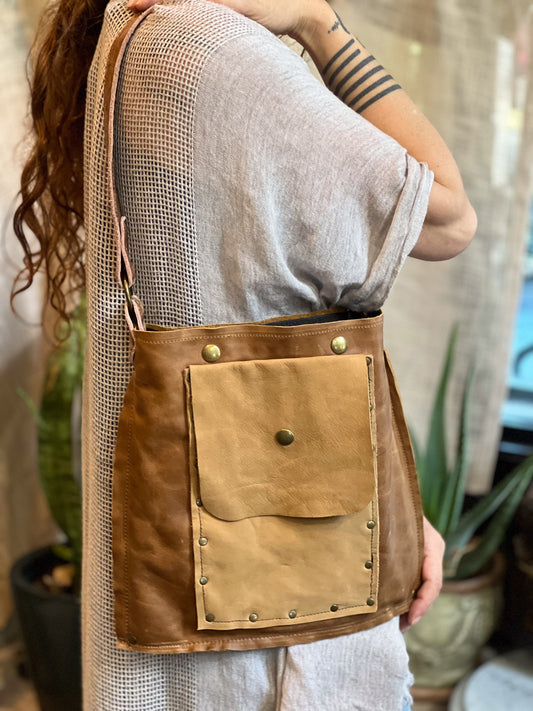 Person wearing a brown leather crossbody bag with mesh back, standing indoors.