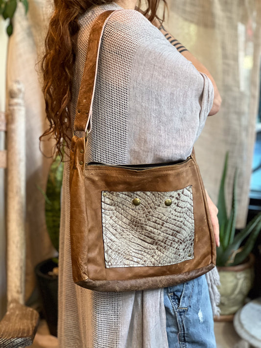 Person wearing a brown leather crossbody bag with decorative patchwork design.