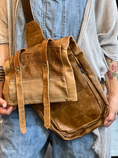 Brown leather bag held by a person wearing a denim apron.