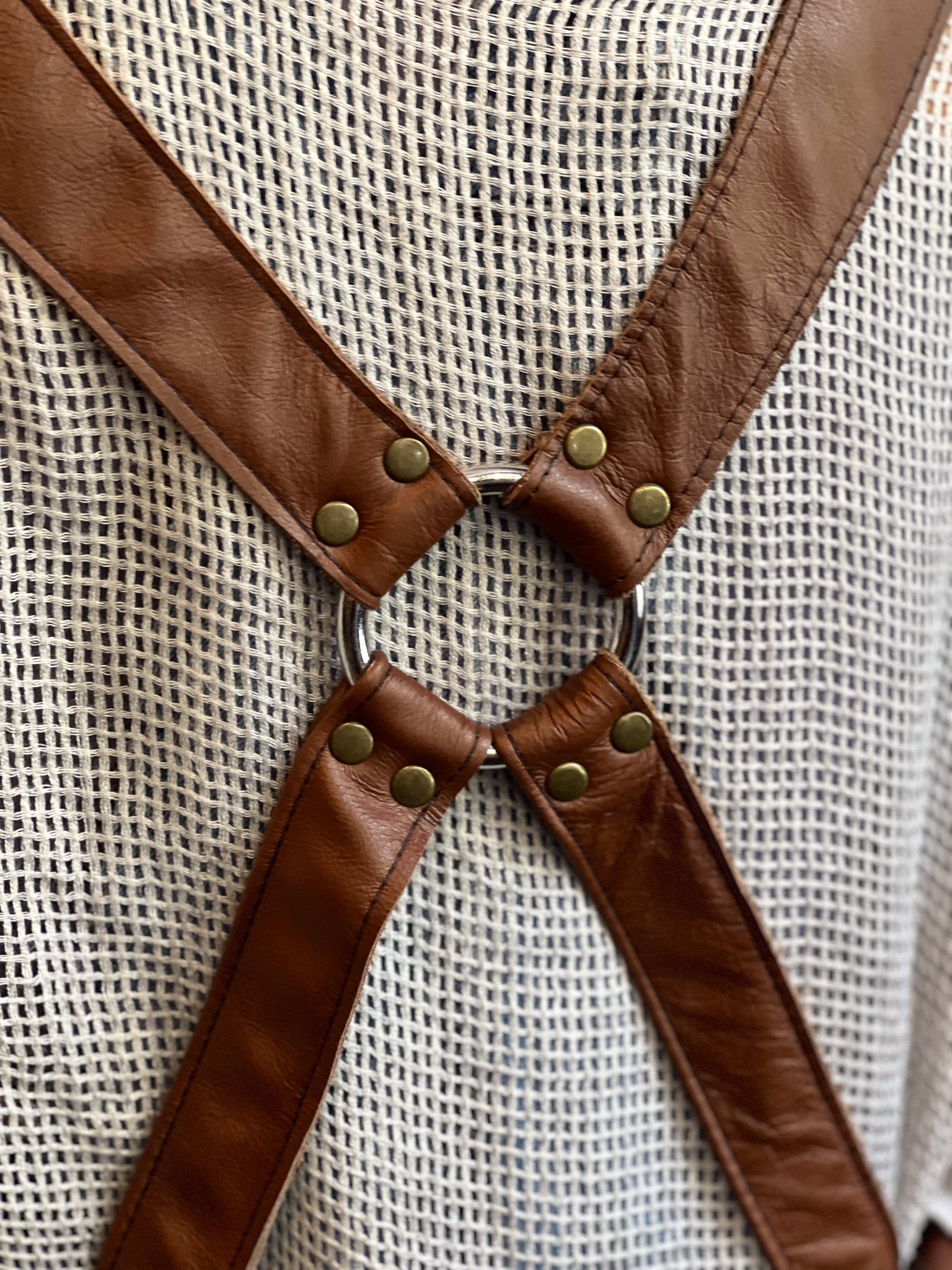 Close-up of brown leather suspenders with metal rings and buttons on a textured beige background.