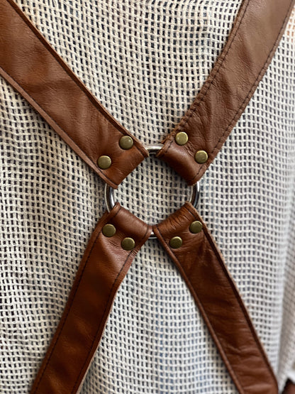 Close-up of brown leather suspenders with metal rings and buttons on a textured beige background.