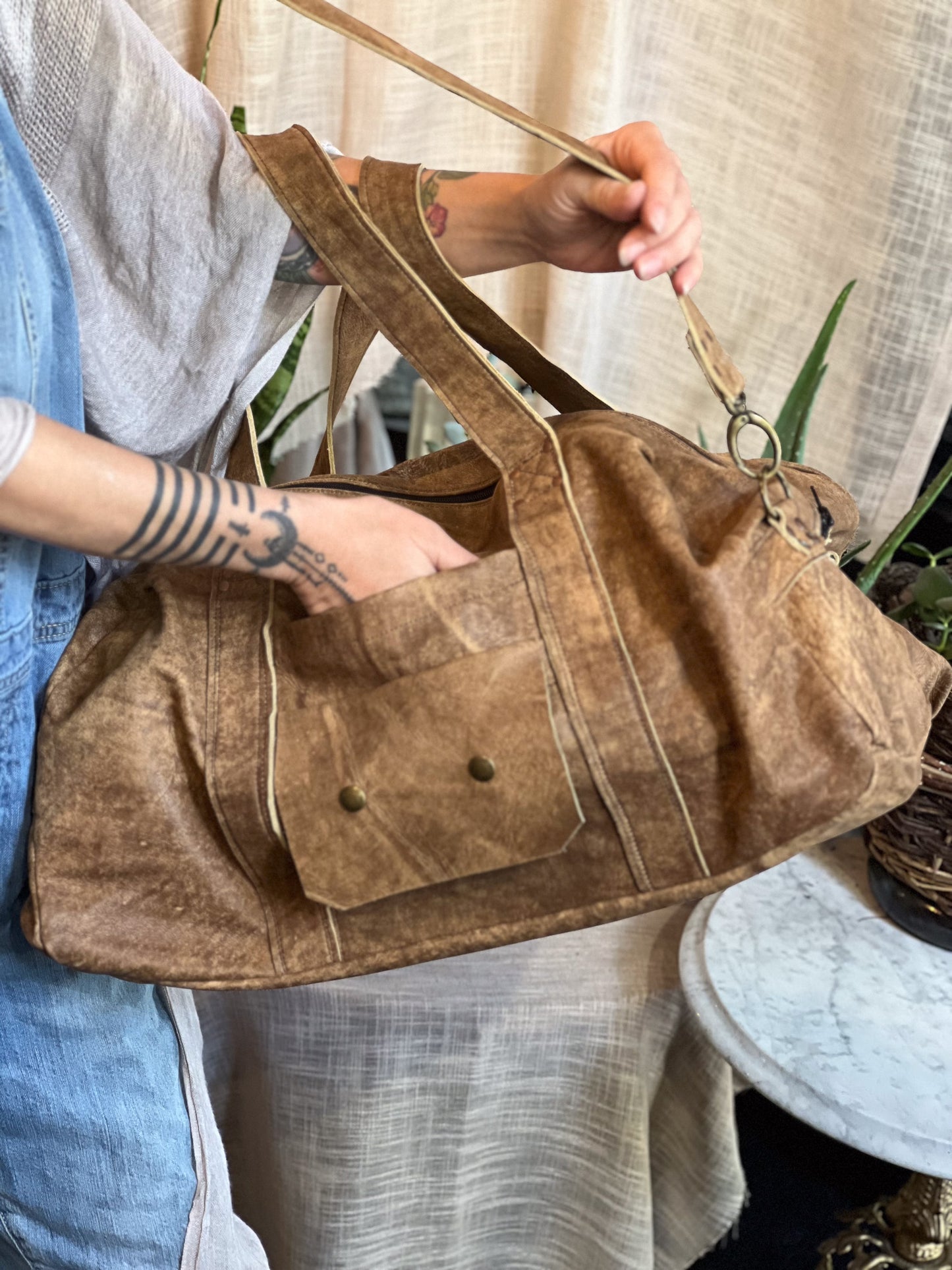 Brown leather bag held by a person with a neutral background