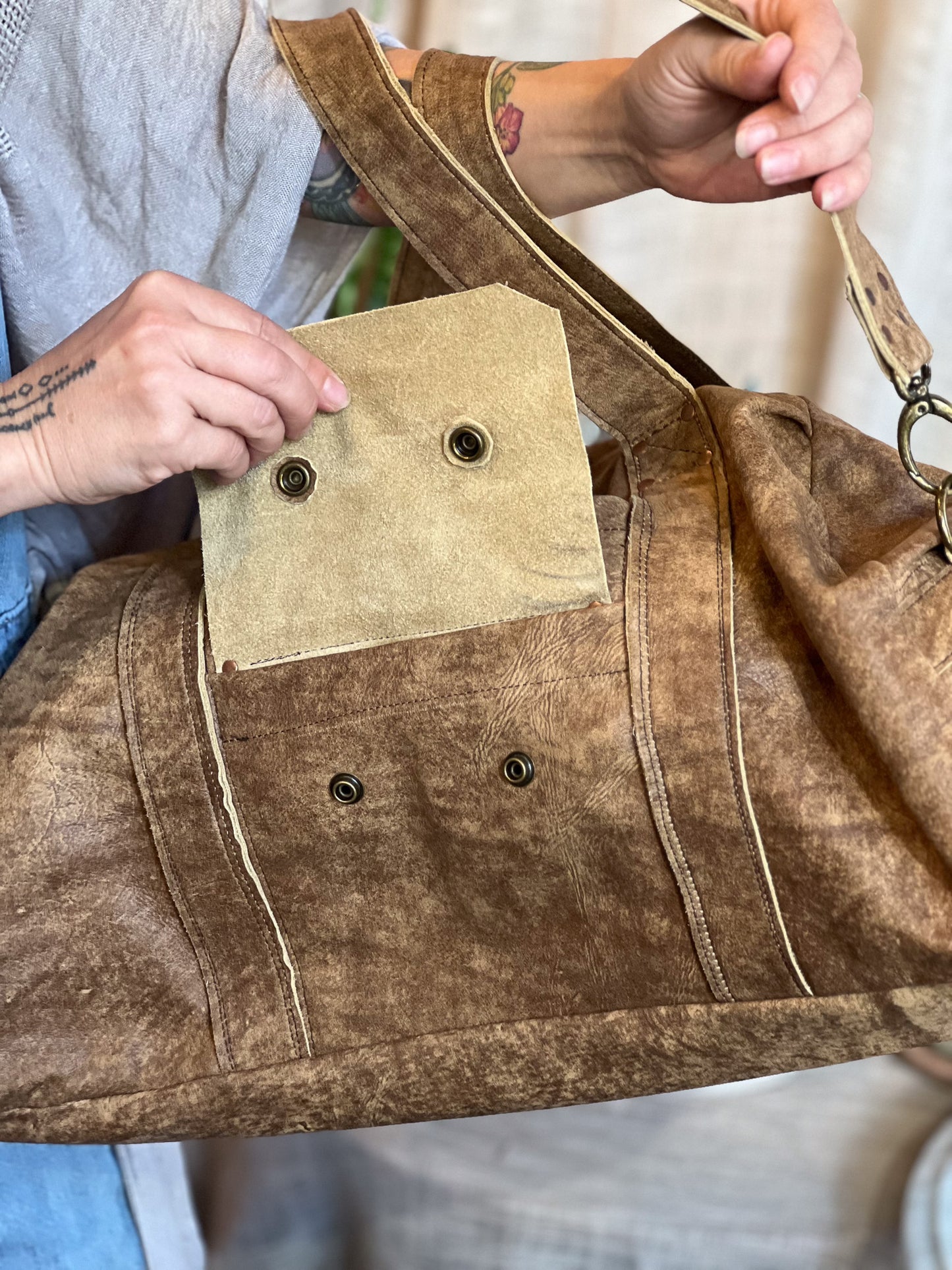 Brown leather bag with a patch and metal buttons held by a person.