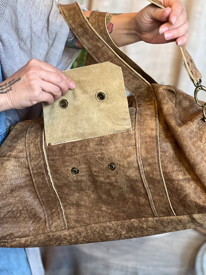 Brown leather bag with a patch and metal buttons held by a person.
