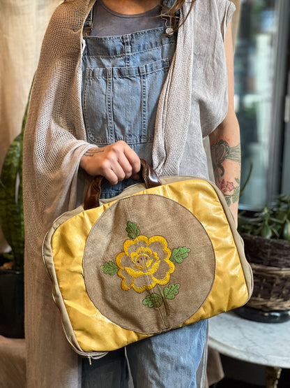 Person holding a yellow bag with floral embroidery in an indoor setting