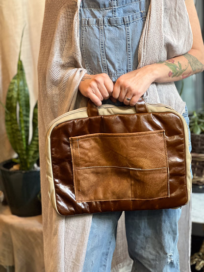 Person holding a brown leather bag with a neutral background
