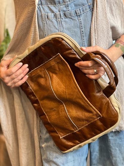 Brown leather bag held by a person wearing a beige cardigan and blue jeans.