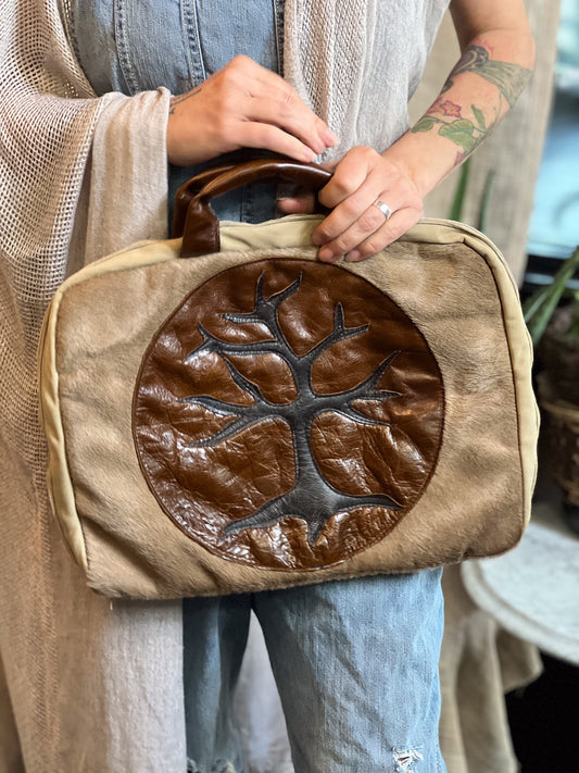 Person holding a brown bag with a tree design, wearing a beige cardigan and blue jeans.