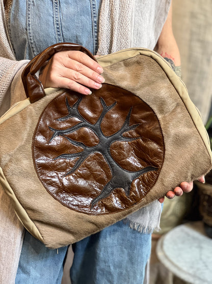 Person holding a brown leather bag with a tree design