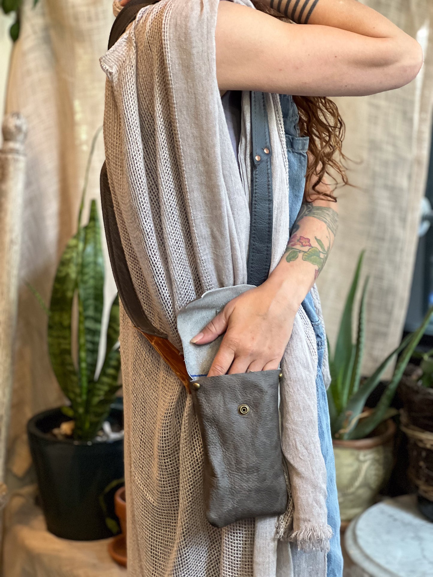 Person wearing a beige cardigan with a gray pouch, surrounded by plants.