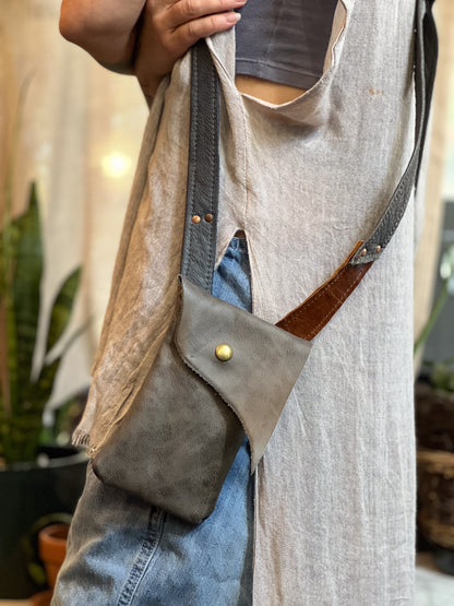Person wearing a light gray vest with a dark brown leather crossbody bag.