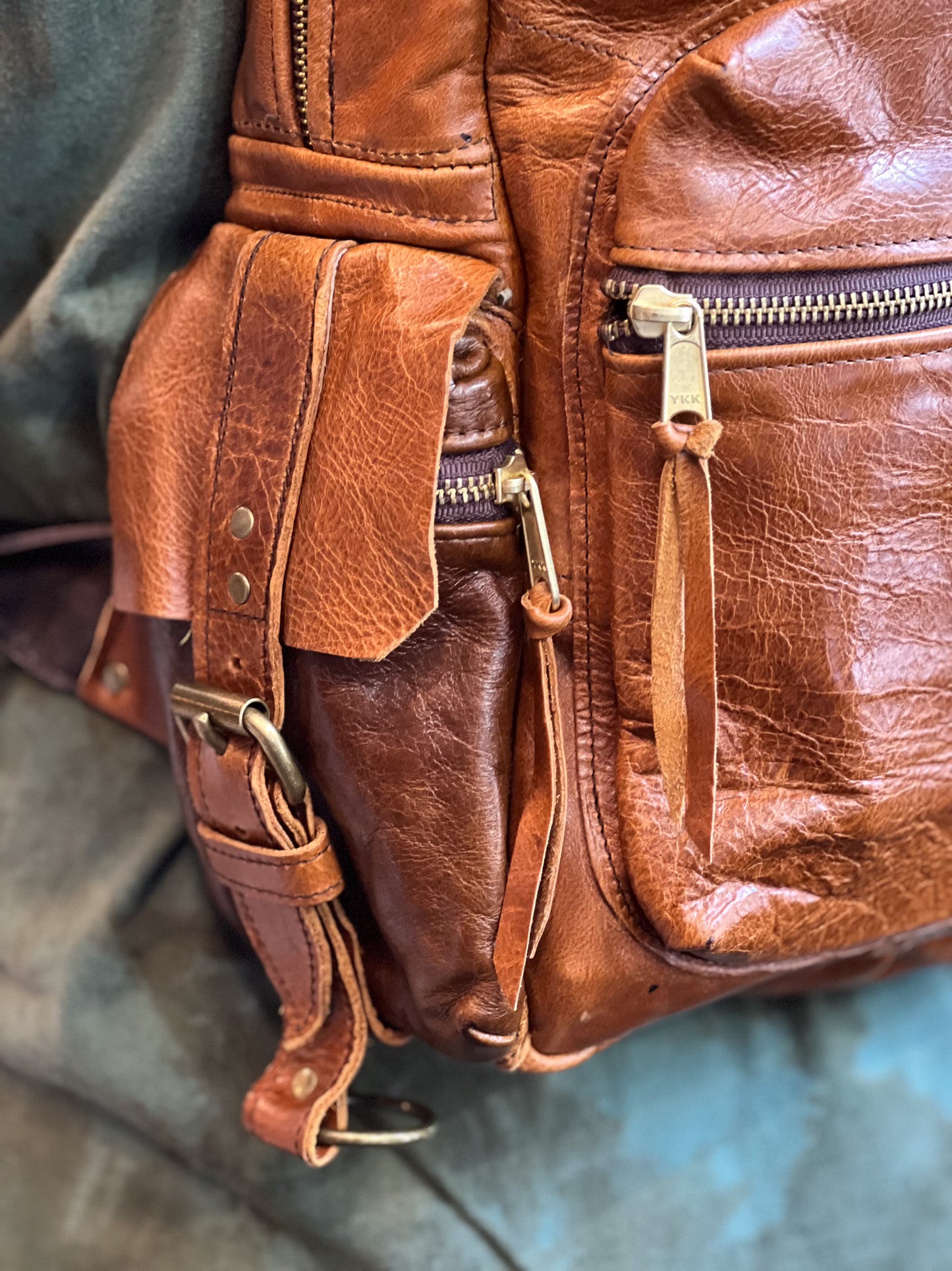 Close-up of a brown leather bag with zippers and straps on a gray background
