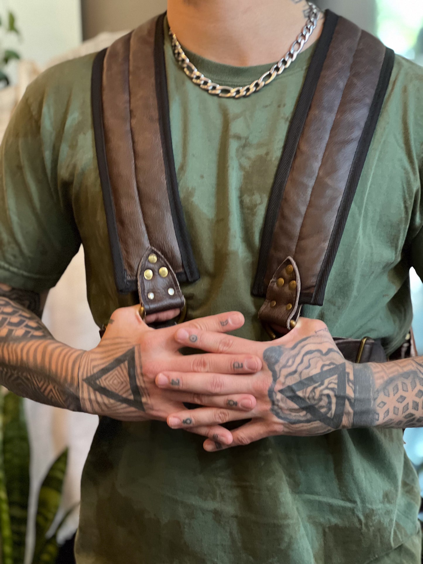Person wearing a green shirt and brown suspenders with tattoos on arms and hands.
