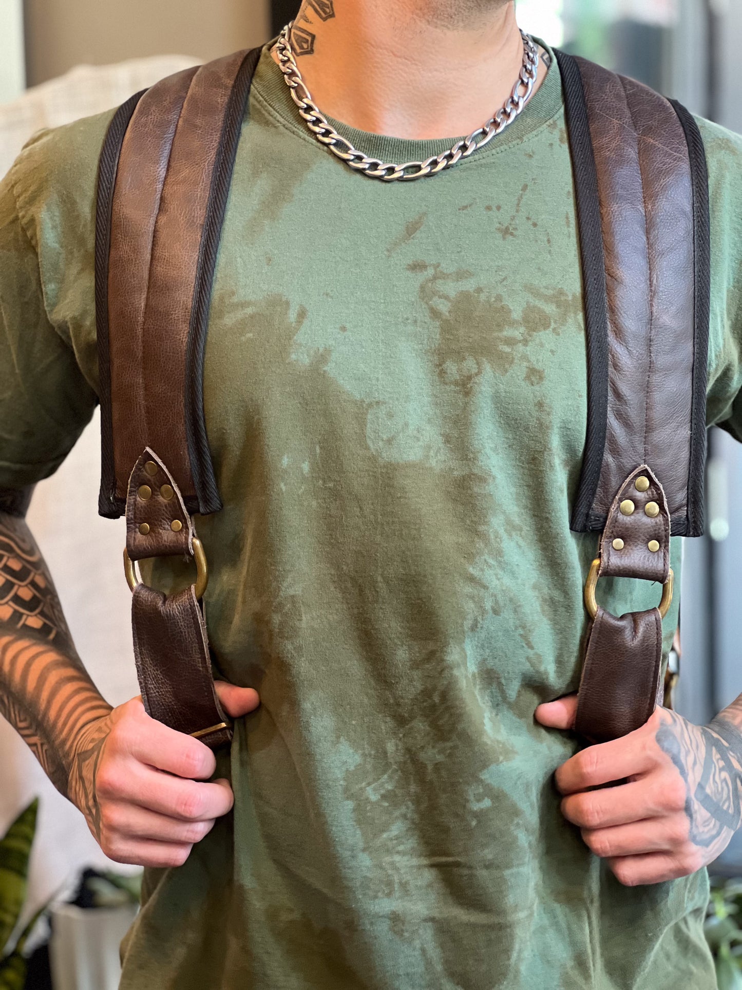Person wearing a green shirt and brown leather suspenders with a blurred background