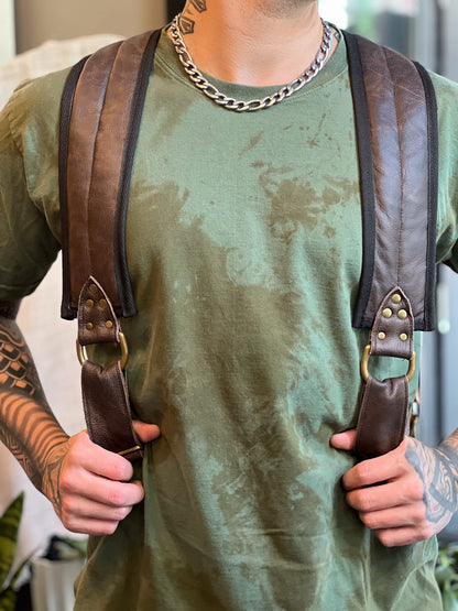 Person wearing a green shirt and brown leather suspenders with a blurred background