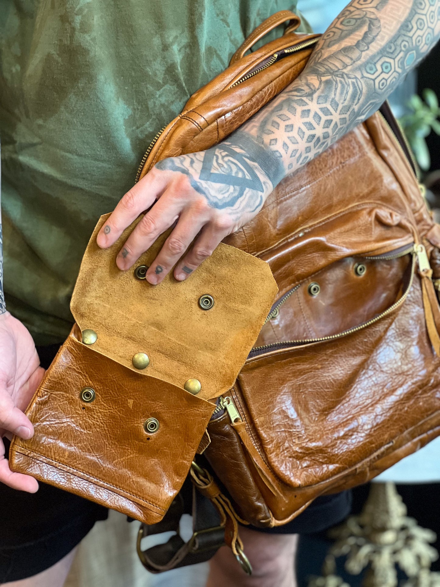 Brown leather bag held by a person with tattoos on their arm.