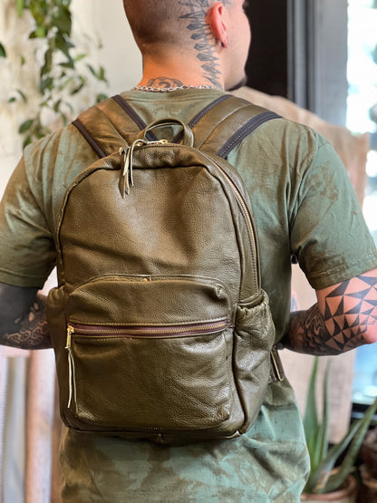 Person wearing a green leather backpack with tattoos on arms and neck.