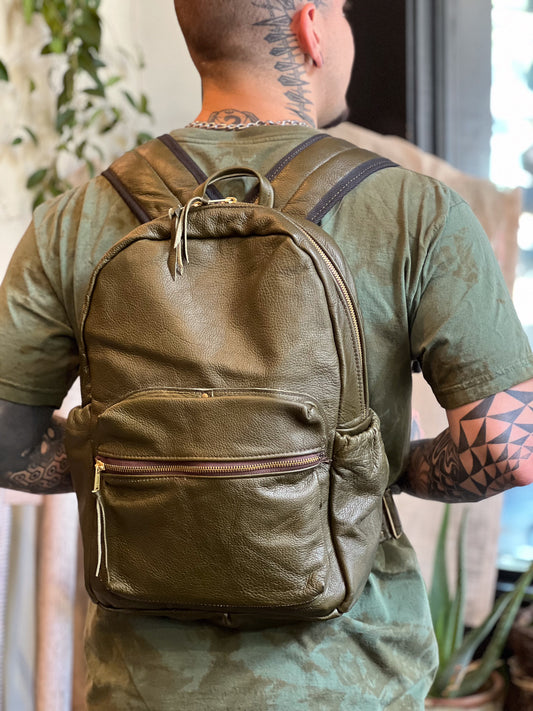 Person wearing a green leather backpack with tattoos on arms and neck.