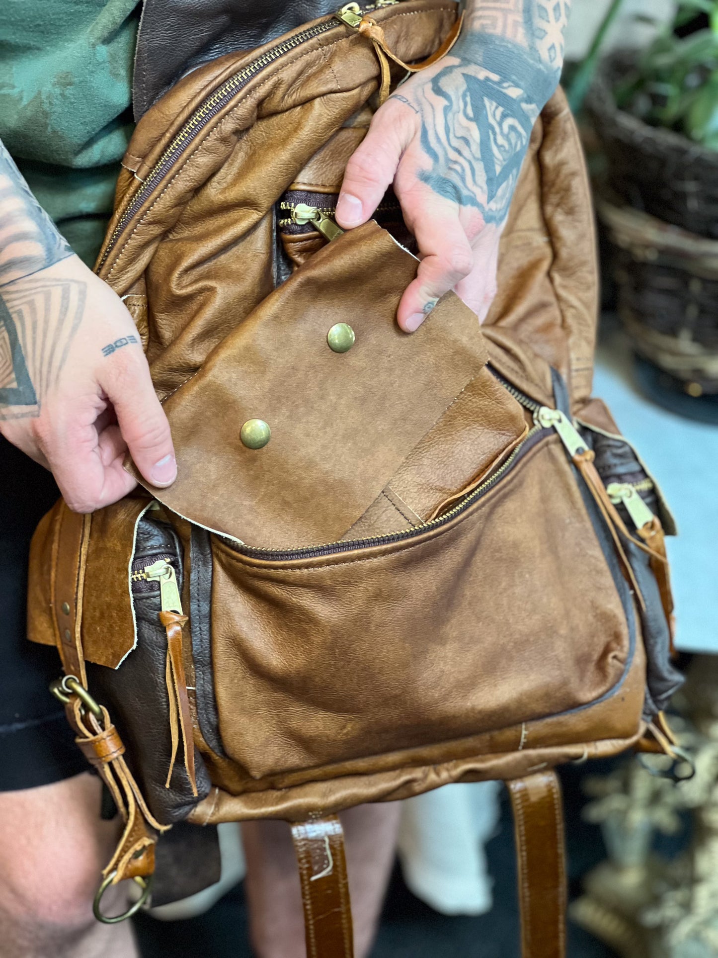 Brown leather bag with green buttons held by a person with tattoos.