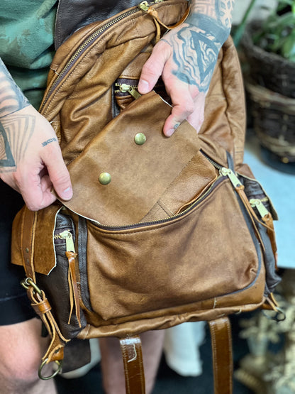 Brown leather bag with green buttons held by a person with tattoos.