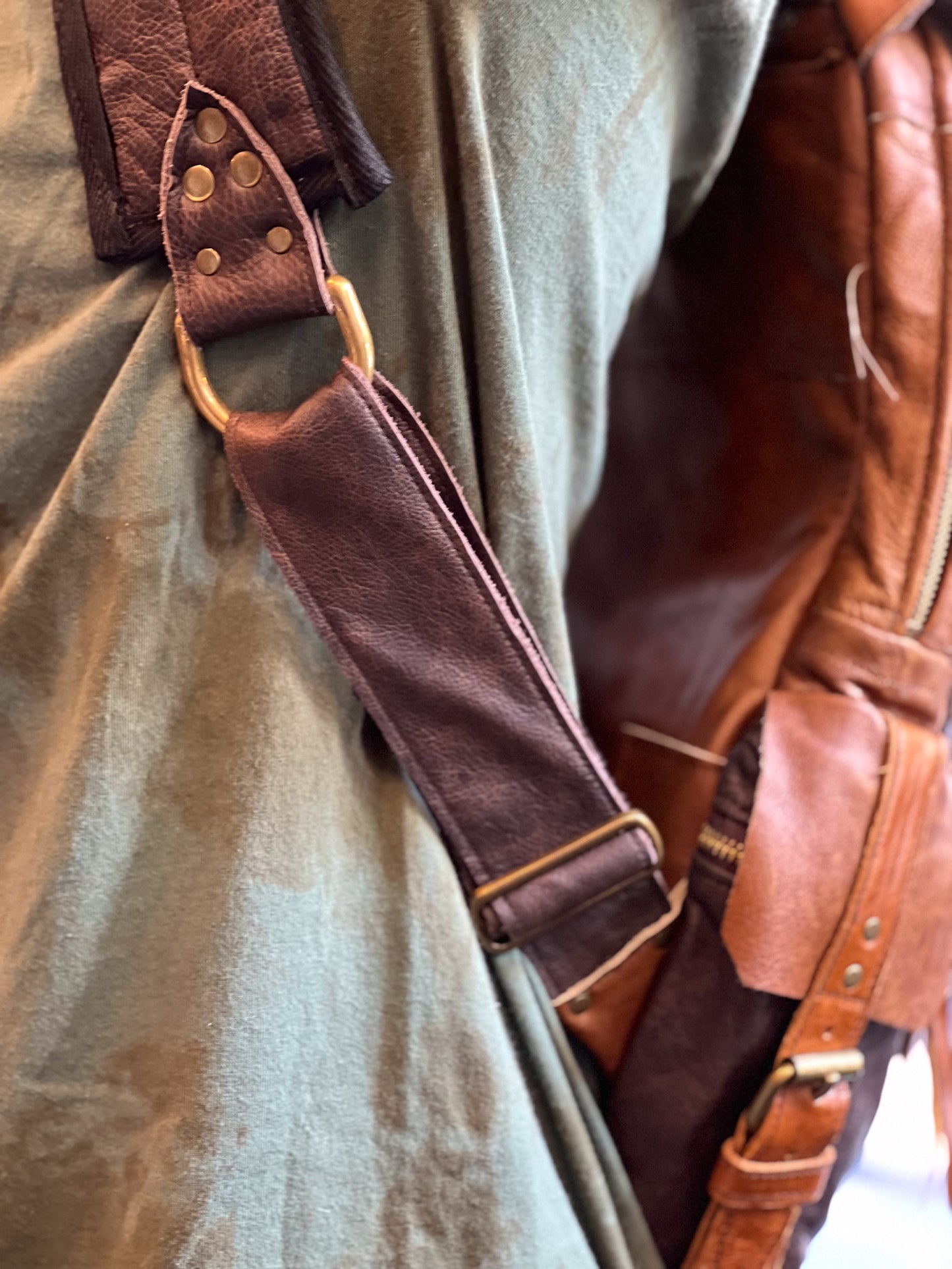 Close-up of a brown leather strap with gold hardware on a green fabric background