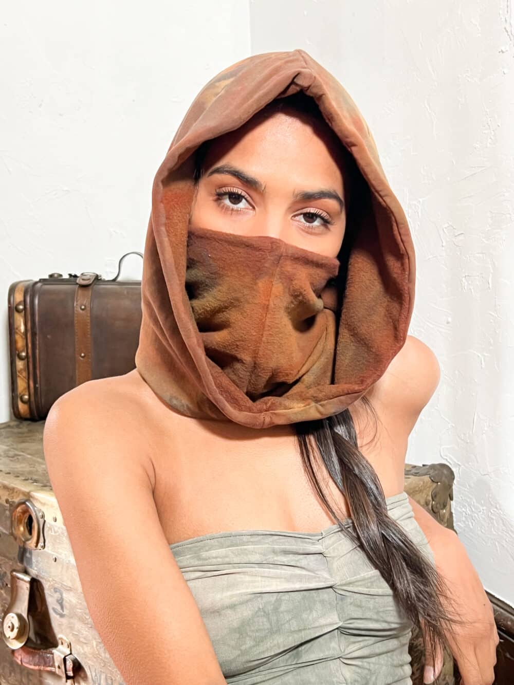 A woman model showcasing a unisex red bamboo fleece, standalone hood; She is wearing the hood and has the entrance to the hood turned inward, and pulled up over her face like a mask.