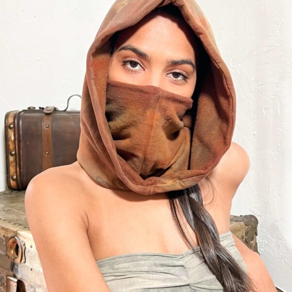 A woman model showcasing a unisex red bamboo fleece, standalone hood; She is wearing the hood and has the entrance to the hood turned inward, and pulled up over her face like a mask.
