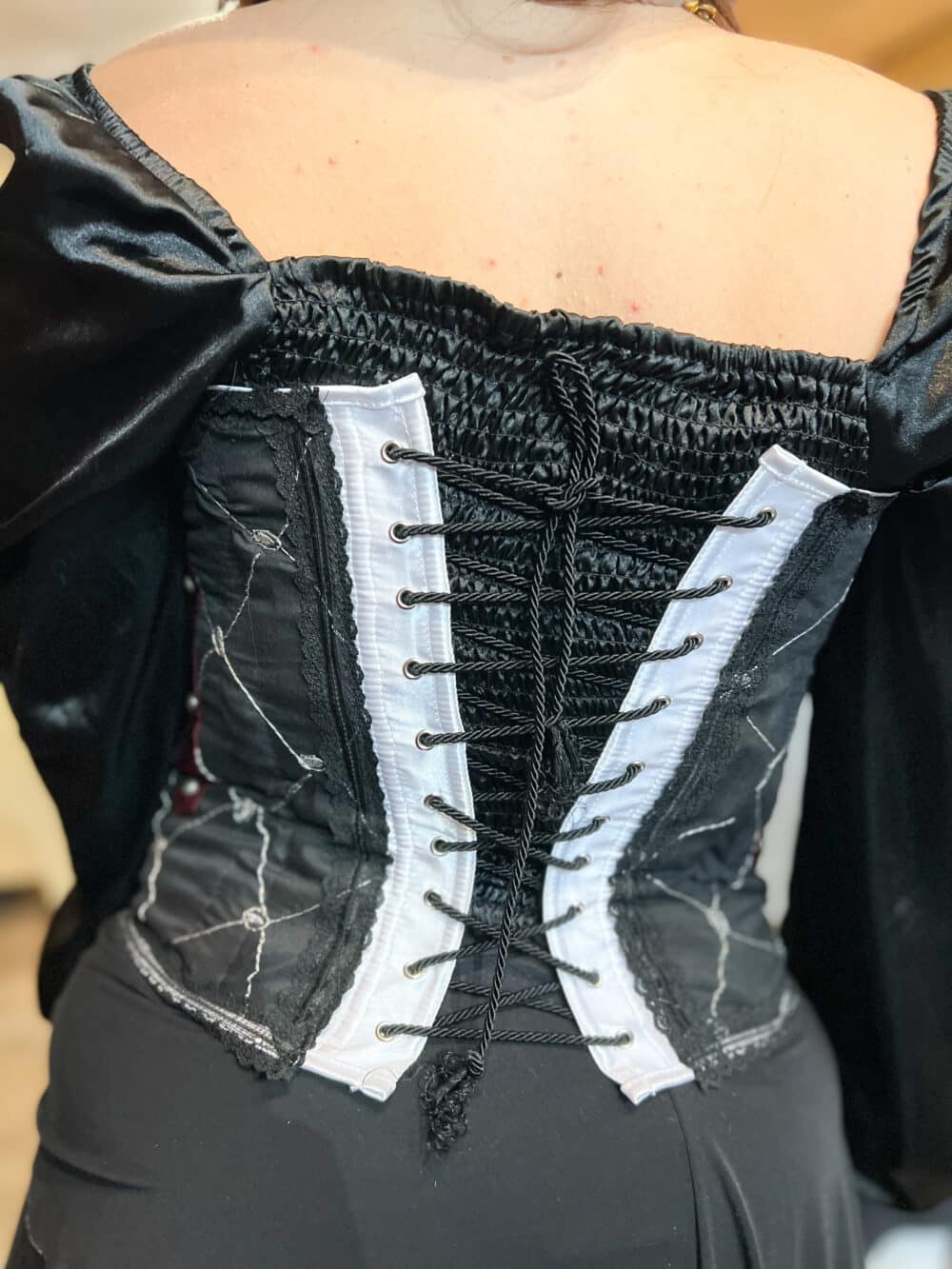 A Victorian Vintage Corset with black textile base, burgundy fabric accents and black lace trim. The corset cinches with black chord.