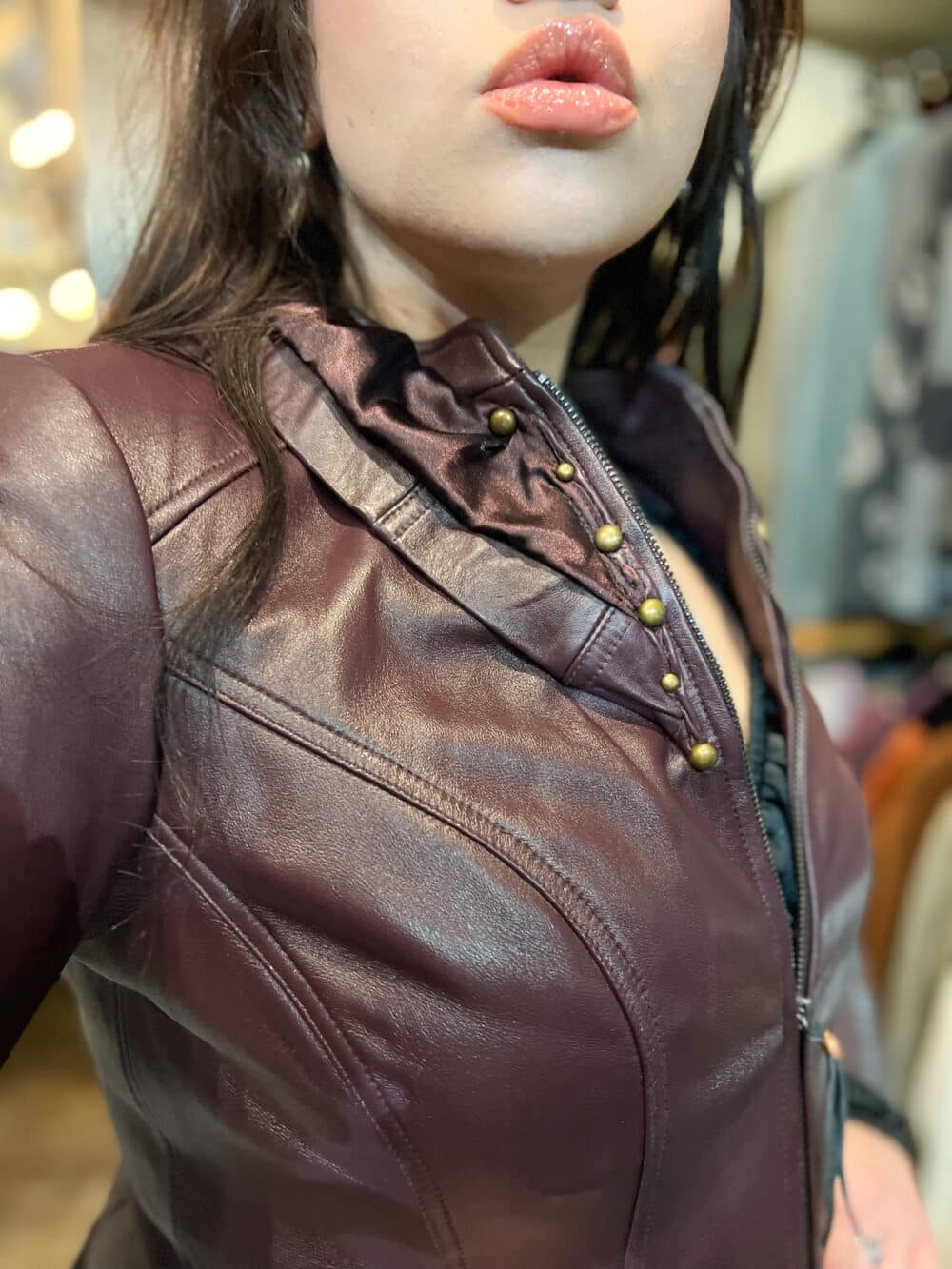 The lapel of a burgundy leather motorcycle jacket. Antiqued brass studs embellish over the lapel.